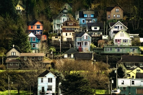 Colorful houses stacked on a hillside, surrounded by trees and greenery, creating a charming neighborhood scene.
