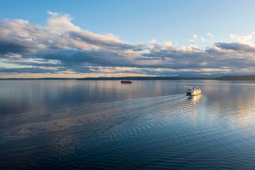 A boat glides across a calm lake under a sky filled with clouds, reflecting the warm light of sunset.