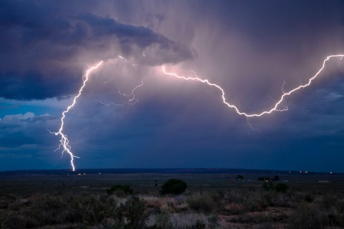 A dramatic lightning strike illuminates a dark, stormy sky over a vast, open landscape.