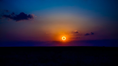 A stunning sunset with a glowing ring around the sun, set against a deep blue sky and wispy clouds.