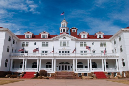 Historic white hotel with a red roof, multiple flags, and a grand entrance under a blue sky.