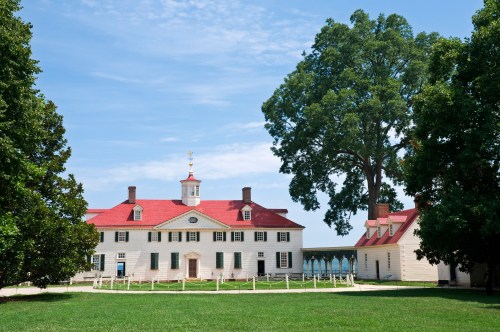 Historic plantation house with a red roof, surrounded by green grass and trees under a blue sky.