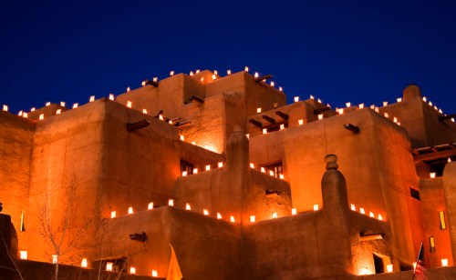 A adobe-style building illuminated by numerous glowing lanterns against a deep blue evening sky.