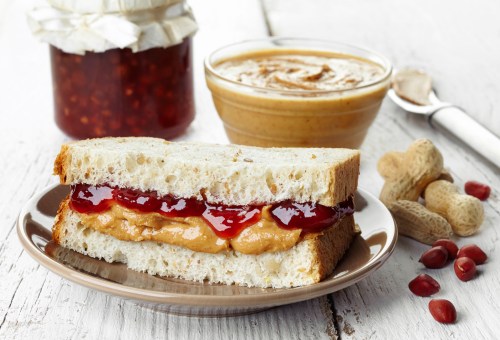 A peanut butter and jelly sandwich on a plate, with a jar of jelly and a bowl of peanut butter in the background.