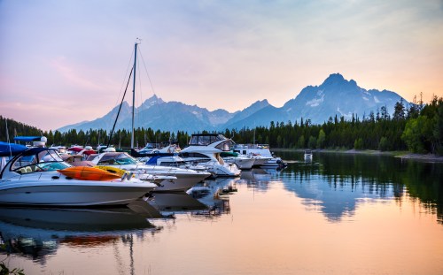 Boats docked at a serene lake with mountains in the background during sunset, reflecting on the water.