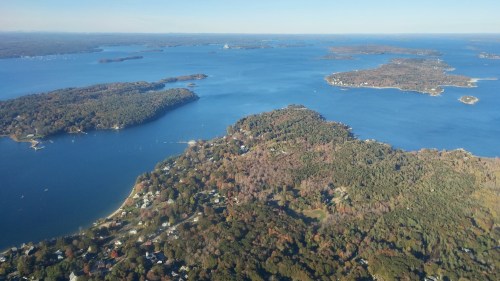 Aerial view of a scenic lake surrounded by islands and wooded areas, showcasing vibrant autumn foliage.