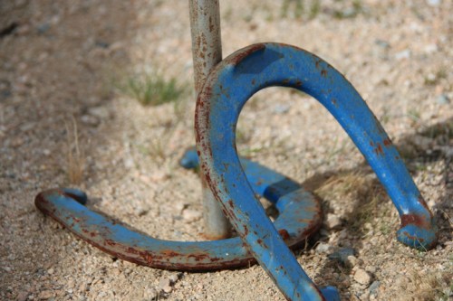 Close-up of rusty blue horseshoes resting on gravel, with a metal post in the background.