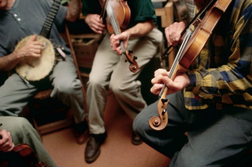Musicians playing string instruments, including a banjo and violins, in a cozy indoor setting.