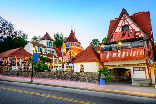 Charming alpine-style buildings with colorful roofs and flags, illuminated at dusk along a quiet street.