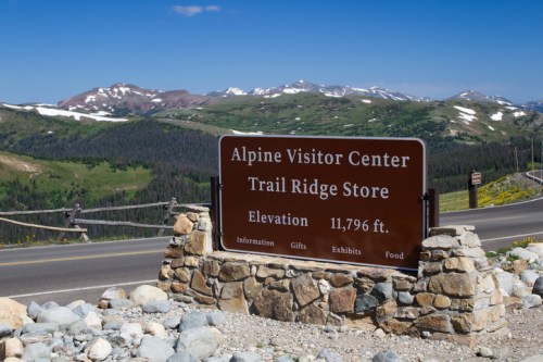 Sign for Alpine Visitor Center and Trail Ridge Store at 11,796 ft elevation, surrounded by mountains and greenery.