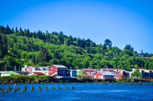 A scenic view of a waterfront town with colorful buildings, surrounded by lush green hills under a clear blue sky.