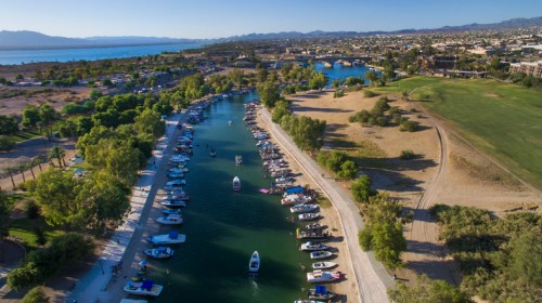 Aerial view of a marina with boats along a green river, surrounded by trees and a scenic landscape.