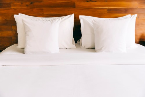 A neatly made bed with white pillows against a wooden headboard.