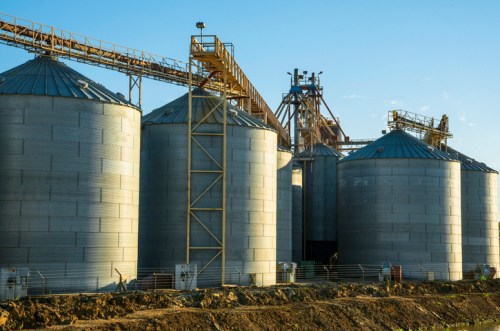 Grain silos with metal structures and machinery against a clear blue sky.