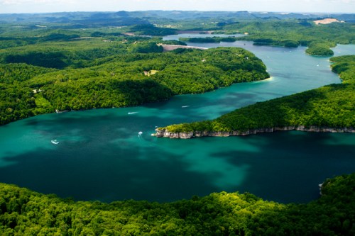 Aerial view of lush green islands and blue waters, surrounded by hills and trees under a clear sky.