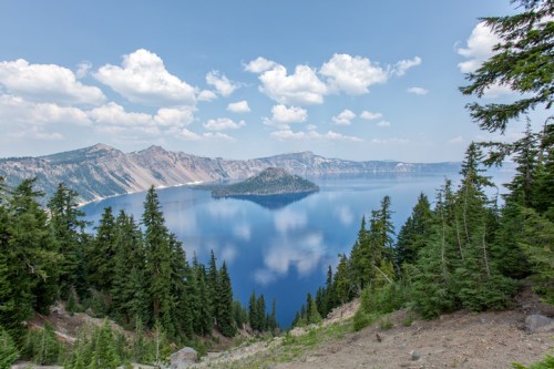 A scenic view of Crater Lake, featuring a deep blue lake surrounded by mountains and lush green trees under a cloudy sky.