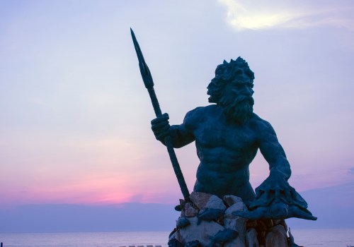 A bronze statue of Neptune holding a trident, set against a colorful sunset over the ocean.