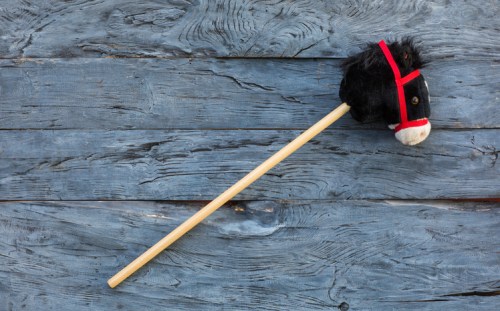 A toy horse head on a stick, featuring a black mane and red bridle, resting on a weathered wooden surface.