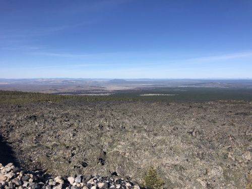 A panoramic view of a vast, rocky landscape under a clear blue sky, with distant mountains on the horizon.