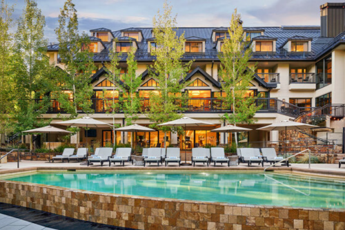 A luxurious hotel with a pool and lounge chairs, surrounded by trees and a scenic backdrop.