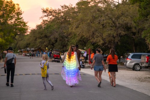 A group walks down a road at sunset, with one person in a colorful, illuminated outfit and children nearby.