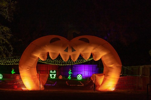 A large inflatable pumpkin archway lit up at night, surrounded by colorful Halloween decorations.