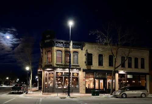 A historic brick building at night, illuminated by streetlights and a full moon, with snow on the ground.