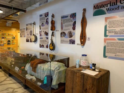 Display of musical instruments and informational panels in a museum setting, with a glass case and wooden table.