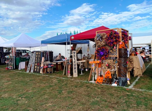 A vibrant outdoor market with colorful tents, handmade crafts, and seasonal decorations, set against a blue sky.