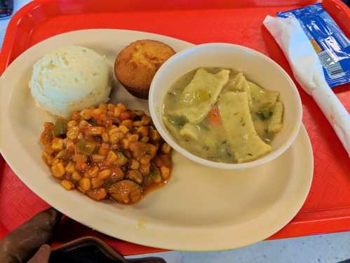 A tray with mashed potatoes, cornbread, a bowl of chicken and dumplings, and a serving of mixed beans.