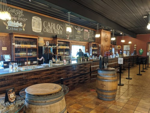 Interior of Carlos Creek Winery featuring a wooden bar, wine bottles, and patrons enjoying the tasting experience.