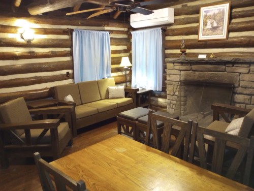 Cozy log cabin interior with wooden furniture, a stone fireplace, and blue curtains. Warm and inviting atmosphere.