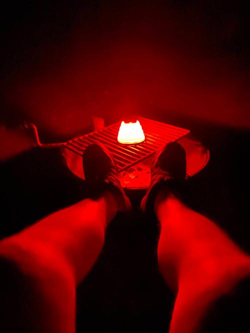 A pair of feet in sneakers resting on a surface, illuminated by a glowing red light.