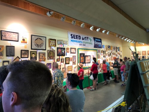 A crowd views various artworks displayed at the Seed Art exhibit at the Minnesota State Fair.