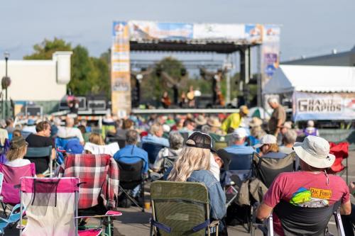 A crowd of people sitting in chairs, enjoying a live music performance on an outdoor stage.