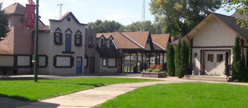 A sunny view of a park featuring buildings with unique architecture and green grass in the foreground.