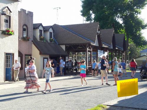 A lively street scene with people walking, shops, and outdoor seating under sunny skies.