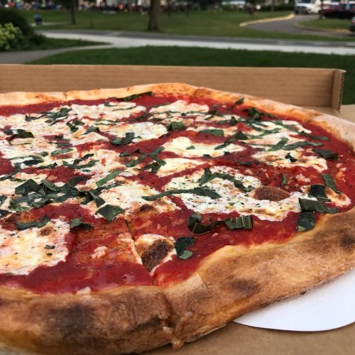 A close-up of a freshly baked pizza topped with tomato sauce, mozzarella, and fresh basil, in a cardboard box.