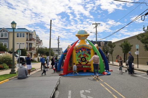A colorful inflatable bounce house on a street, with children playing and adults supervising under a partly cloudy sky.