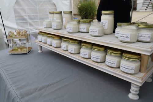 A display of jars filled with various creams and candles on a wooden shelf at a market.
