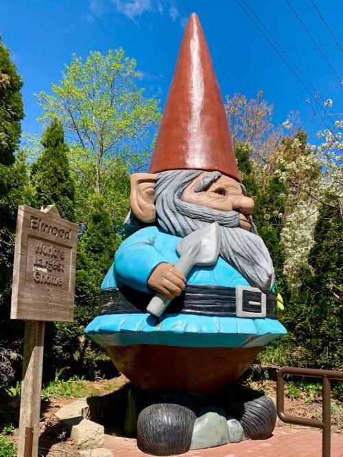 A large, colorful gnome statue holding a tool, next to a sign that reads "Elwood, World's Largest Gnome."