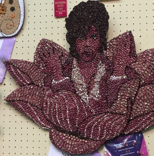 Art piece featuring a figure resembling a person surrounded by a lotus flower, made from various seeds and beans.