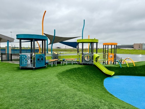 Colorful playground equipment with slides and climbing structures on green turf under a cloudy sky.