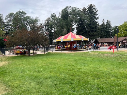 A colorful carousel in a park, surrounded by trees and people enjoying the attractions on a sunny day.