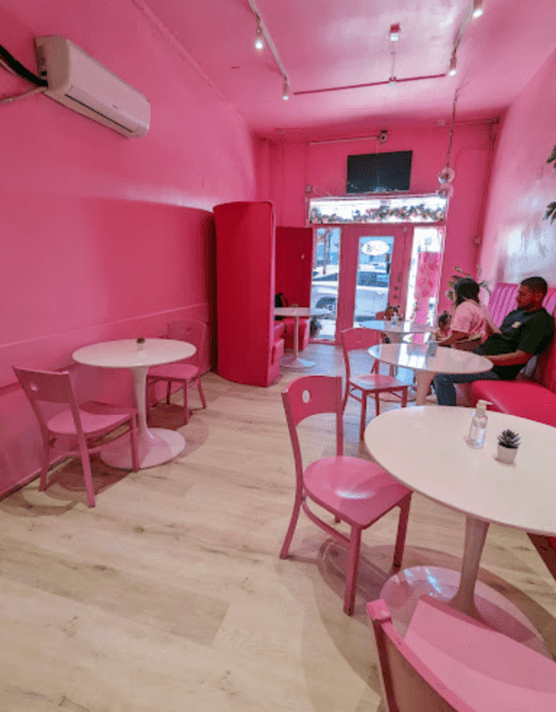 A bright pink cafe interior with two tables, pink chairs, and a couple sitting together near the entrance.
