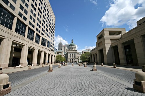 View of a wide street lined with buildings, leading to a dome-topped government building under a blue sky with clouds.