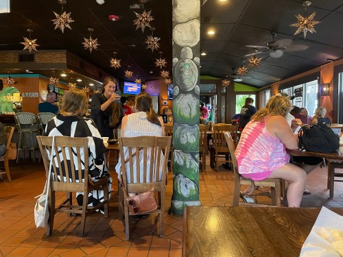 A busy restaurant interior with patrons seated at wooden tables and a server interacting with customers.