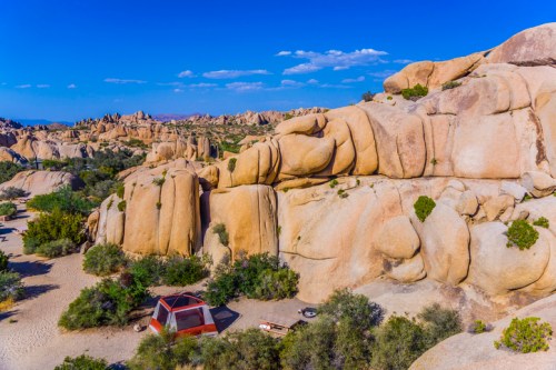 A scenic view of large rock formations and a red tent in a desert landscape under a clear blue sky.