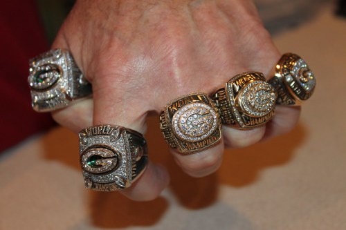A hand displaying five championship rings, each adorned with diamonds and featuring the words "World Champion."
