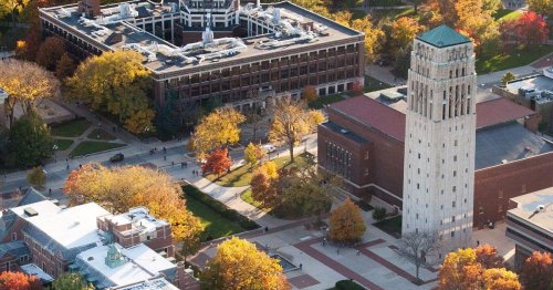 Aerial view of a university campus with colorful autumn trees and notable buildings, including a clock tower.